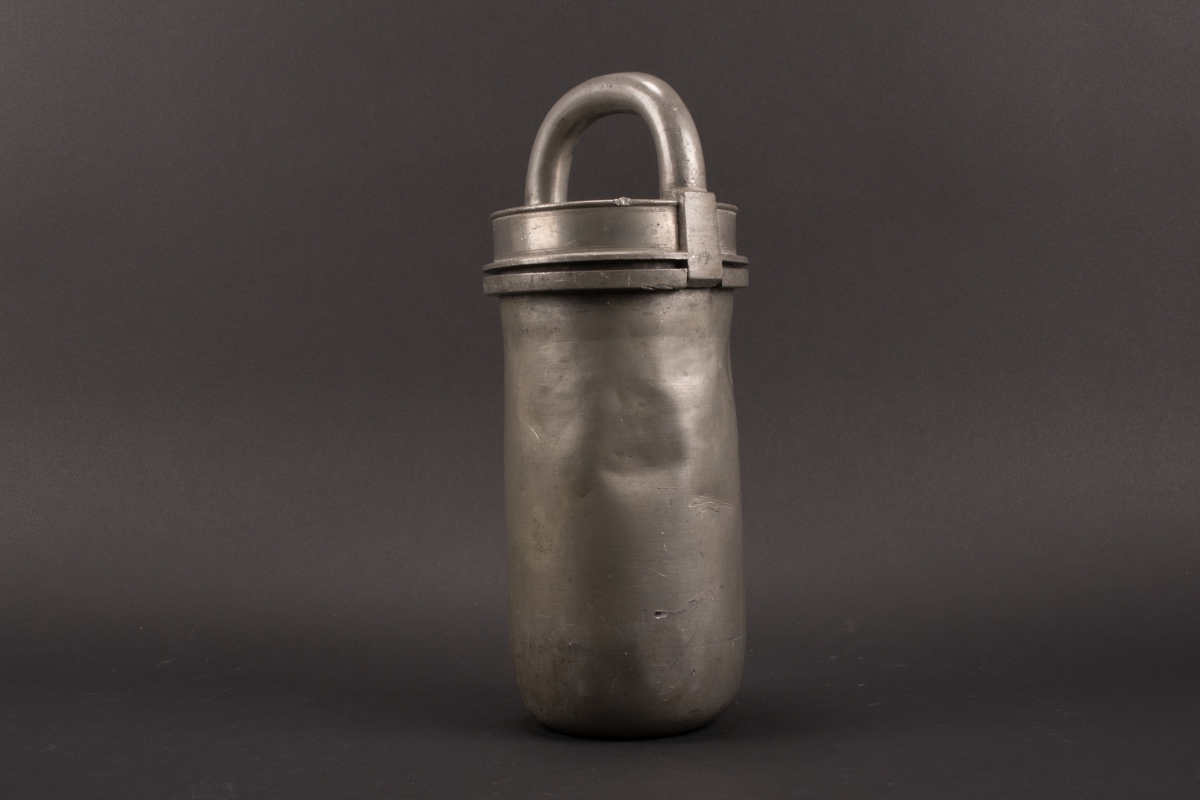 Cylindrisk glassform av tenn. Lock med halvcirkelformat handtag. Formens botten är något rundad.