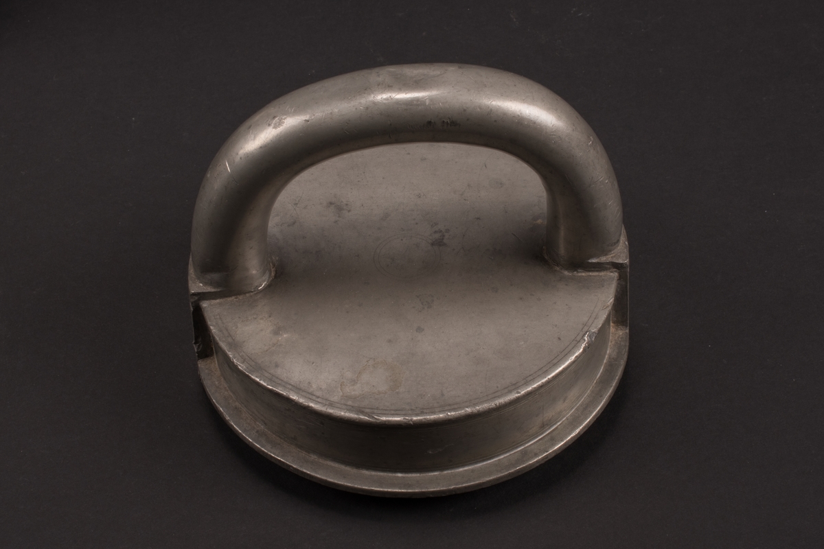 Cylindrisk glassform av tenn. Lock med halvcirkelformat handtag. Formens botten är något rundad.