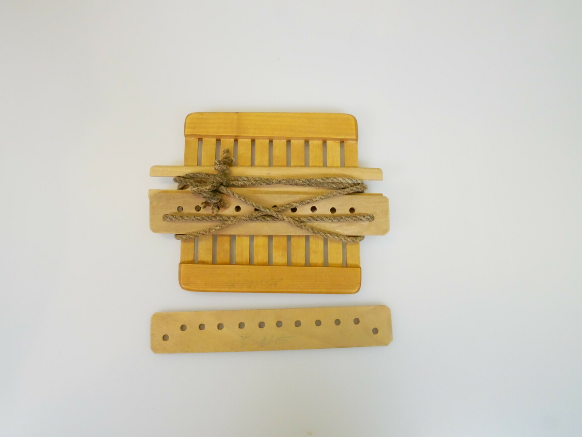 Rektangulært vevgrind i tre som består av fire deler. En plate med 10 spiler festet til treplater i begge endene. Spilene har små hull midt på. Tre små treplater, to med 12 små hull, og med innhakk på begge kortsidene. Ett brunt bånd er festet rundt grindvev