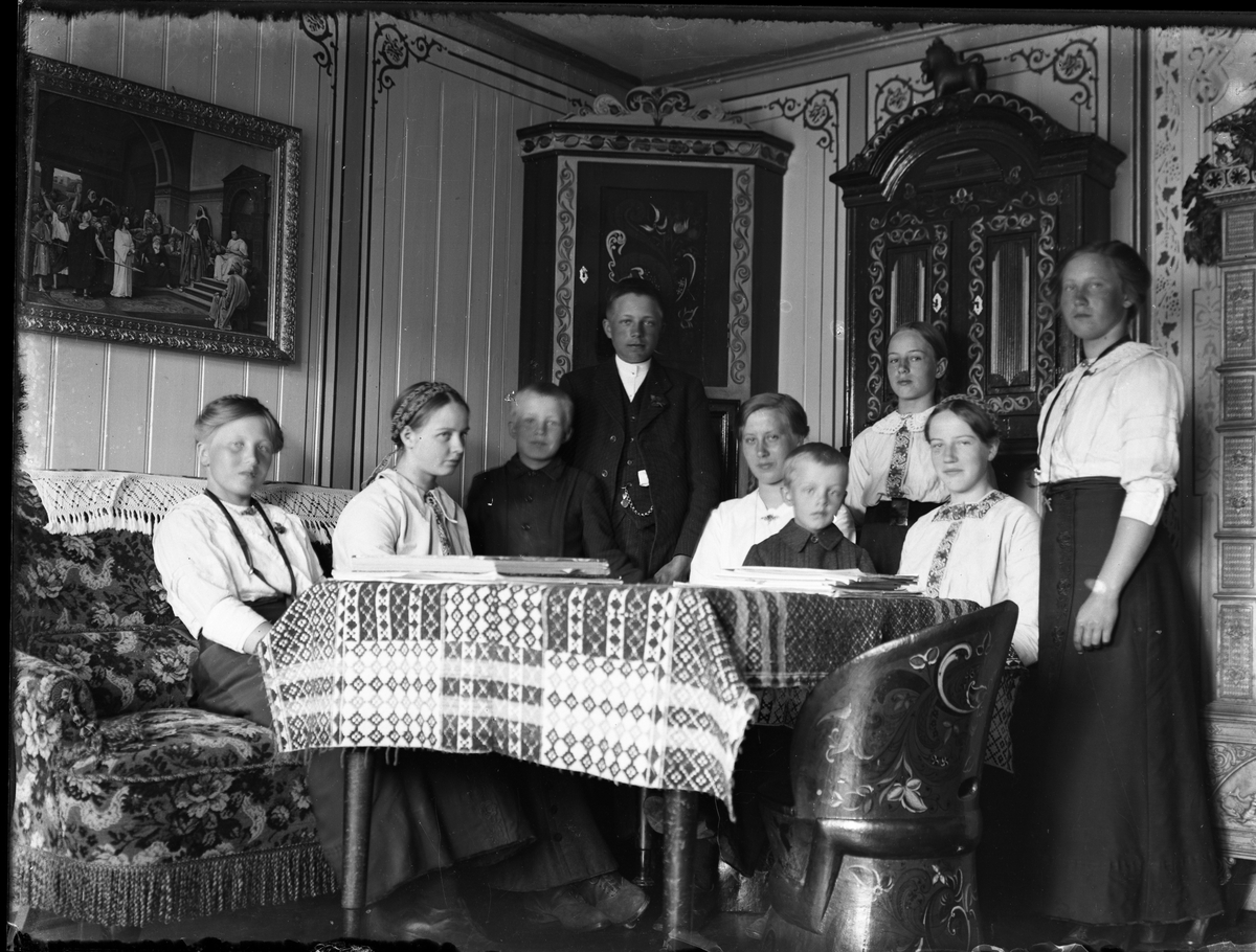 Fotosamling etter Bendik Ketilson Taraldlien (1863-1951) Fyresdal. Gårdbruker, fotograf og skogbruksmann. Fotosamlingen etter fotograf Taraldlien dokumenterer områdene Fyresdal og omegn. 
Gruppeportrett med barn og ungdom i stua på Taraldlien.