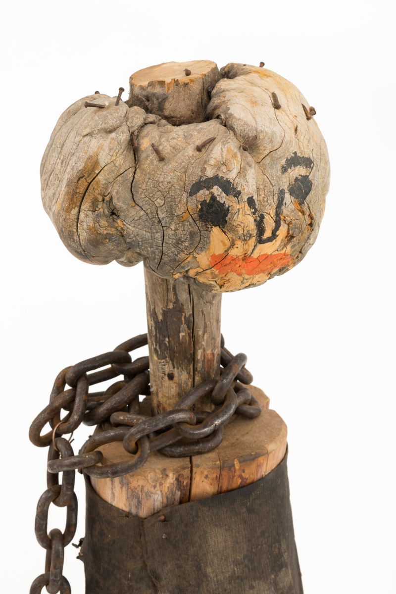 Menneskeliknende figur, i hovedsak lagd av tre. Denne figuren ble periodevis montert i baugen på slepebåten «Trysilknut», der den fungerte som «Osensjøfløternes maskot». Den er laget av mannskapet på slepebåten. Beina på figuren er lagd av en kløftet furustamme - 48-50 centimeter lang og med en diameter på 13-14,5 centimeter i det som en gang var rotenden på treet, men som har blitt overkroppen på figuren, I denne endekabben er det nedtappet en tynnere trestamme (diameter 4,7.5,5 centimeter) med en markant utvekst, ei rikule. Disse komponentene er brukt som henholdsvis hals og hode på figuren. På den ene sida av rikula er det påmalt øyne og nese med svart maling, mens munnen og leppene er antydet med rødt. Øverst på denne komponenten er det en del rustne småskruer, som muligens har vært brukt til å feste en «hårmanke» som ikke lenger er intakt. Figuren har bukser som er lagd av et brunsvart stoff, en slags tynn lærimitasjon. Rundt halsen på figuren er det festet en lensekjetting, som et skjerf.