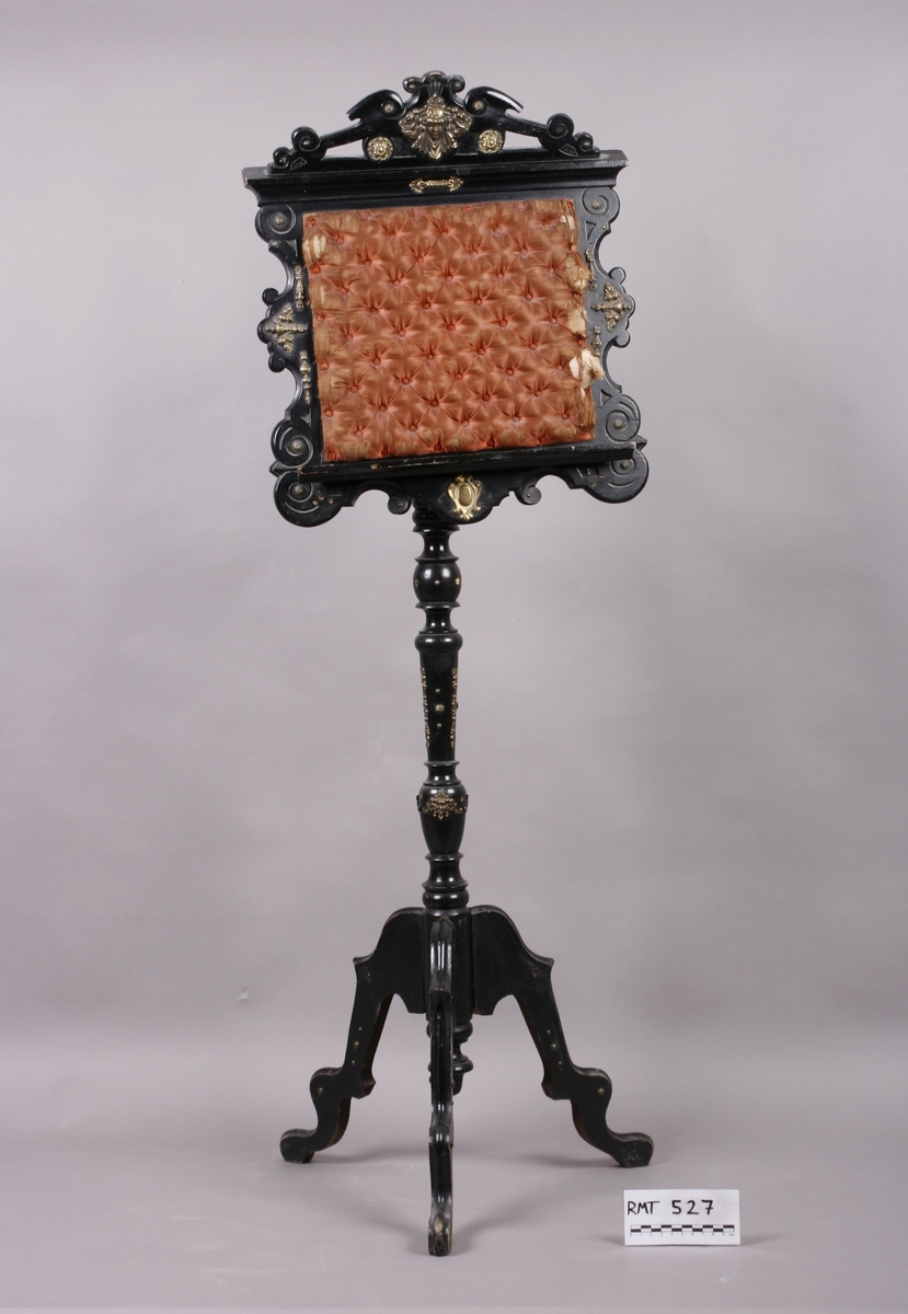 Notestativ i sortmalt tre. Notestol og fot kan settes sammen, foten deler seg i tre nederst. Rike profileringer på fot og stol, messingbeslag som er hamret i naturalistiske og stiliserte ornamenter. Stolen er på forsiden trukket med rustrødt, stoppet sikestoff. Denne kan reguleres på baksiden. Her kan men se merker etter to lister som sannsynligvis er det gamle festet mellom stol og fot.