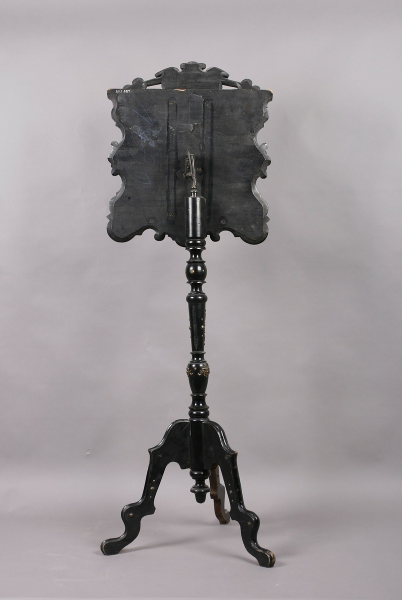 Notestativ i sortmalt tre. Notestol og fot kan settes sammen, foten deler seg i tre nederst. Rike profileringer på fot og stol, messingbeslag som er hamret i naturalistiske og stiliserte ornamenter. Stolen er på forsiden trukket med rustrødt, stoppet sikestoff. Denne kan reguleres på baksiden. Her kan men se merker etter to lister som sannsynligvis er det gamle festet mellom stol og fot.