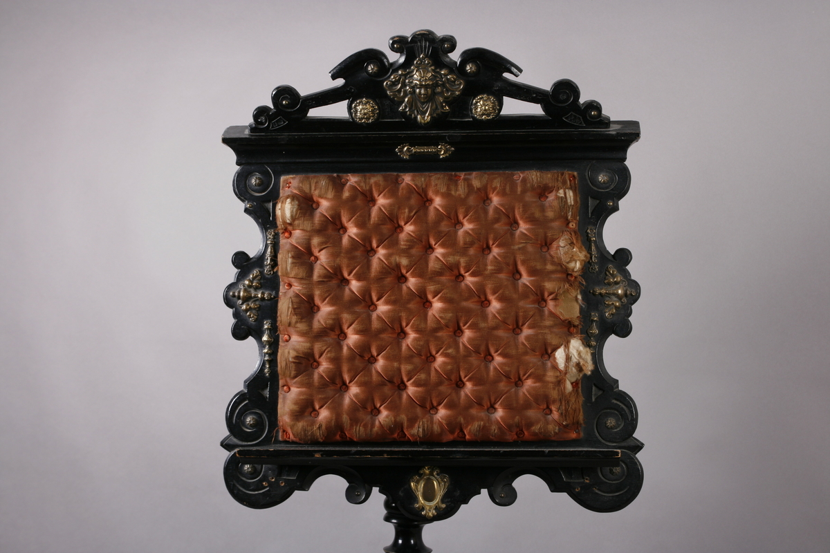 Notestativ i sortmalt tre. Notestol og fot kan settes sammen, foten deler seg i tre nederst. Rike profileringer på fot og stol, messingbeslag som er hamret i naturalistiske og stiliserte ornamenter. Stolen er på forsiden trukket med rustrødt, stoppet sikestoff. Denne kan reguleres på baksiden. Her kan men se merker etter to lister som sannsynligvis er det gamle festet mellom stol og fot.