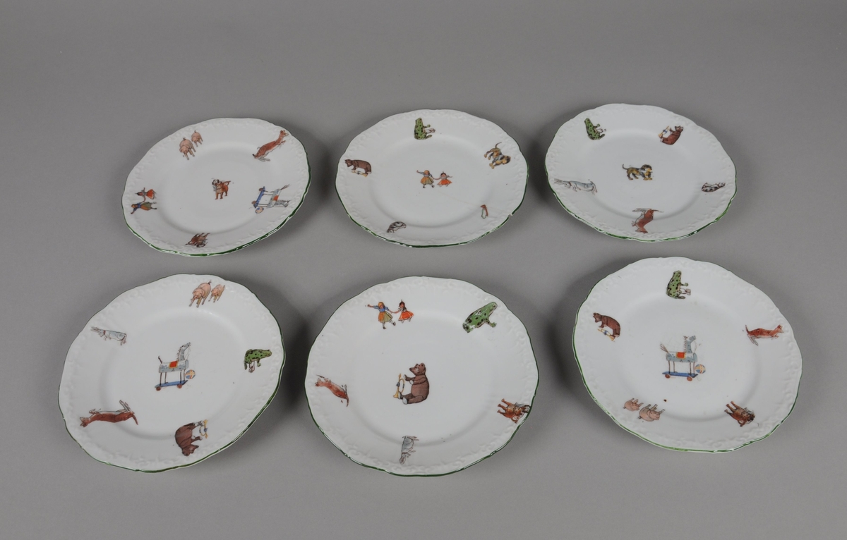 Seks leketallerkener av glassert keramikk. Randen er bølgete og har en dekorativ grønn stripe. Flerfarget trykk med motiv av dyr og leker, hver tallerken har forskjellige kombinasjoner av trykkene.