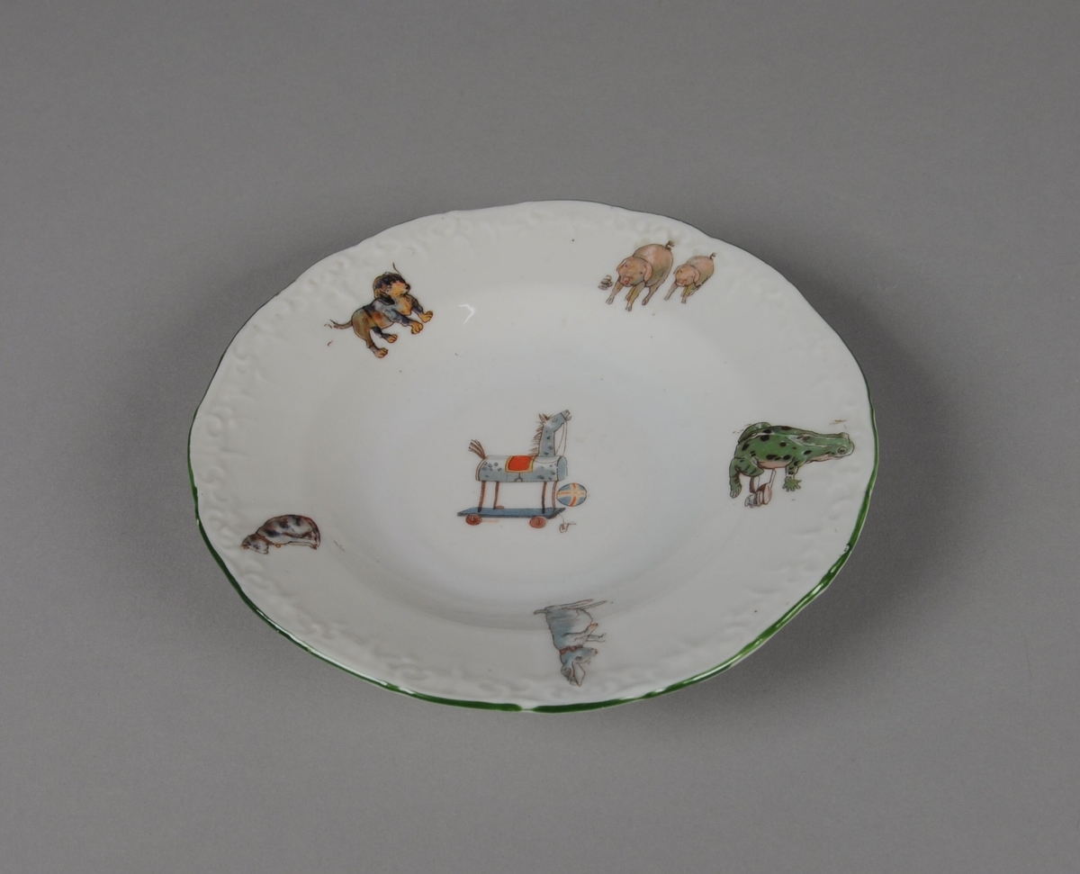 Seks leketallerkener av glassert keramikk. Randen er bølgete og har en dekorativ grønn stripe. Flerfarget trykk med motiv av dyr og leker, hver tallerken har forskjellige kombinasjoner av trykkene.