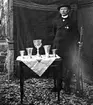 SIGFRID JOHANSSON, RUD, FREDSBERG, VID ETT BORD MED PRISPOKALER O MED ETT GEVÄR I HANDEN, TROLIGEN SKYTTEPRISER