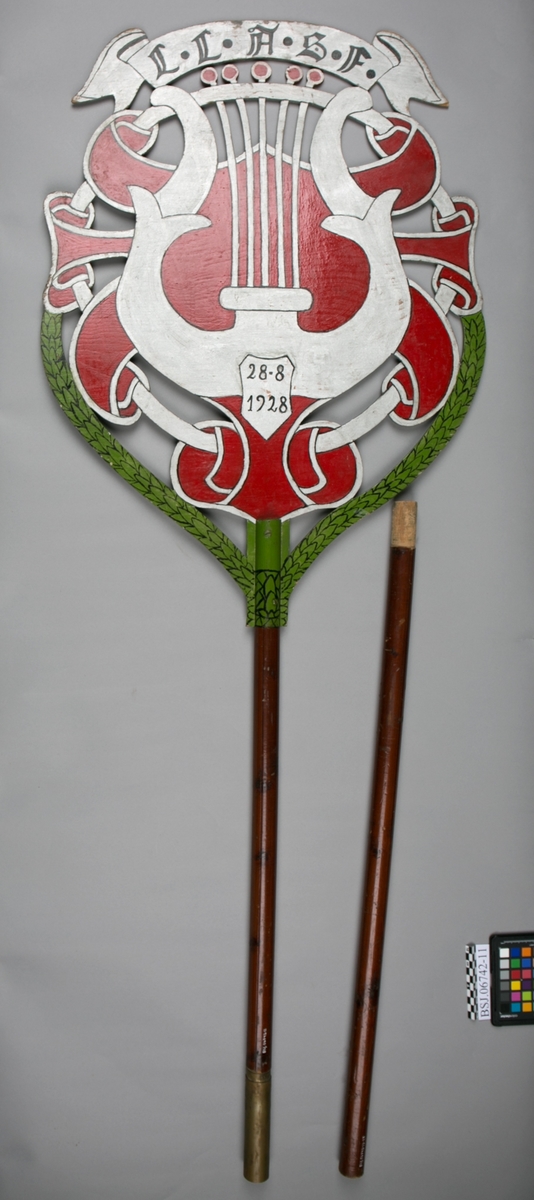Emblem med motiv av strenginstrumnt lyre. Samme motiv på begge sider av emblem.
