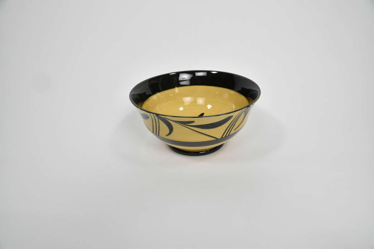 Bolle til mokkaservise, gult med svart pynt, bestående av 30 deler. Serviset er brukt som dokkestell. Dokkestell ble gitt til jenter til lek som forberedelse til voksenlivet. 