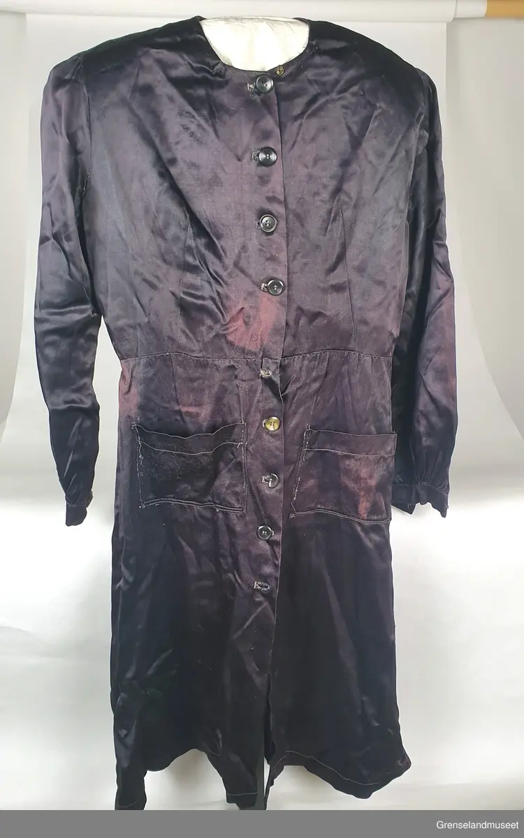 Sprt forkelkjole. Sydd av kåpefor. Bølankt stoff, muligens viskose (kunstsilke). Maskinsydde sømmer, Sårkanter overkastet med hånd. Håndsydde knapphul. Knappene fra kåpa.