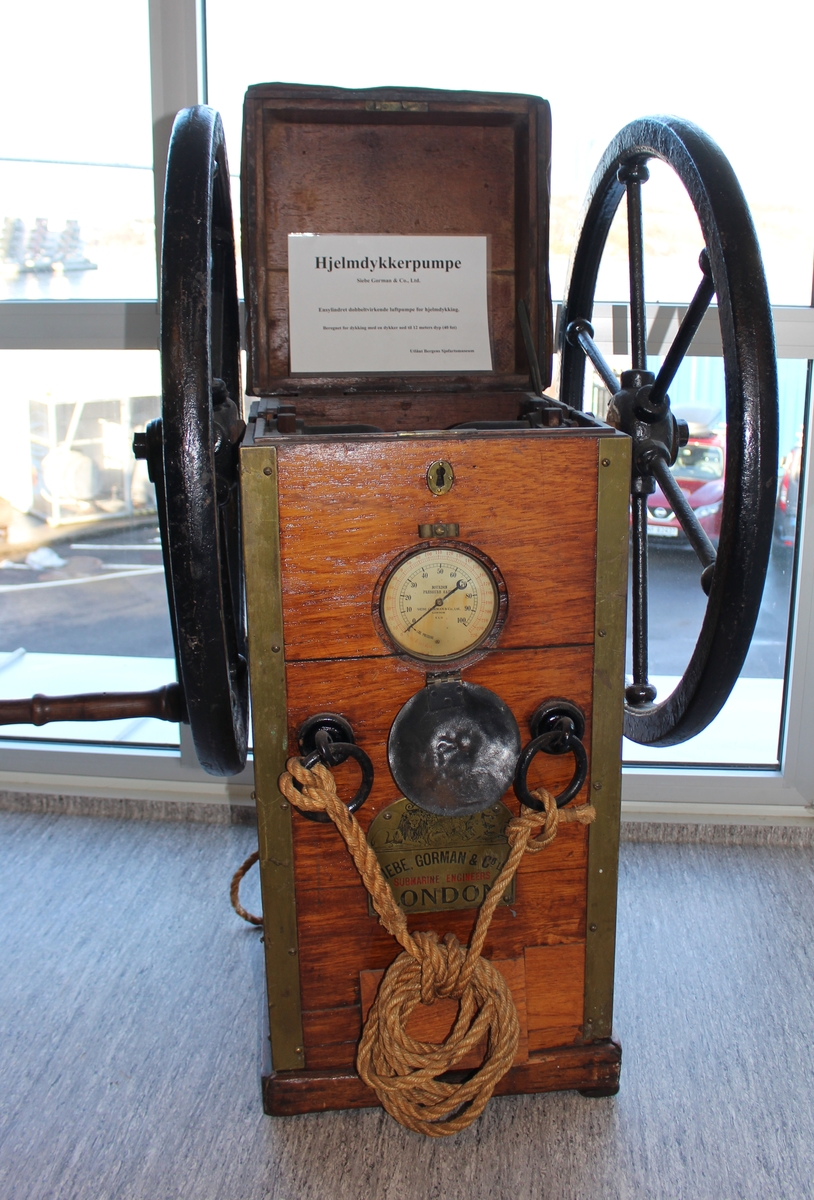 Håndrevet dykkerpumpe type Siebe Gorman. Ensylindret manuell pumpe med to svinghjul med håndtak samt tauverk for løfting av pumpen. Benyttet til å pumpe luft ned til dykkere.