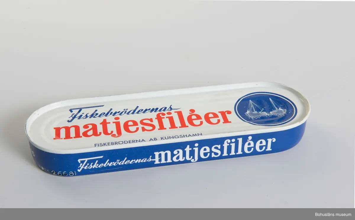 Avlång burk med rundade ändar. Tryckt dekor i blått, vitt och rött. 
Text: "Fiskebrödernas matjesfiléer. Fiskebröderna AB Kungshamn"
I bottnen innehållsförteckning.

Om givaren: Se UM026667.

Under slutet av 1800-talet byggde Kungshamnsskepparen  Hilmer Johansson tre små magasin på Fiskeskär intill sin kaj i Kungshamn. Här bedrev han under 1880-90-talet salteri, tunnbinderi och fraktfart. Bröderna Knut  och Manfred Kristiansson hyrde tillsammans med sin släkting Knut Hedberg ett av magasinsutrymmena på Fiskeskär av Hilmer Johanssons sterbhus och bildade 1920 bolaget Bröderna Kristiansson & Co, som senare blev känt för sina goda inläggningar under namnet Fiskebrödernas Konserver. 1942 bildades aktiebolaget Fiskebröderna AB och sortimentet utökades till hel- och halvkonserv i alla former. 1974 såldes rörelsen till Västkustfisk AB,  men behöll namnet Fiskebröderna AB. Västkustfisk AB  hade ett samarbete med Svenska Västkustfiskarnas Centralförbund SVC. Man fortsatte i oförminskad omfattning och flyttade 1987 rörelsen till Hovenäset och uppköptes av ABBA 1988.

Materialet är insamlat av Bohusläns museum i februari 1988 i samband med att konservfabrikens byggnader revs.

Se även tidigare inv.nr från Fiskebröderna AB: UM24171 - UM24185, UM24191, UM24192.

Material om konservindustrin i Bohuslän är arkiverad under Dokumentation-och Kulturminnesvårdsavdelningen med seriesignum M7D.
Se även tidningsartikel om sortimentet i Bilagepärmen, UM15081.

Litteratur: Bohusläns samhälls- och näringsliv. 4. Konservindustrin.  (1983)  Bohusläns museum, Etnologiska institutionen vid Göteborgs universitet, Landstinget i Göteborgs och Bohus län.
Kungshamn, Gravarne - Bäckevik och Fisketången genom seklerna. Arbetsgruppen för Kungshamnsboken. Uddevalla 1996.
Ur hav till burk och kartong. Fiskberedningen i Sotenäs kommun. Projekt Sverige i Blixtbelysning. Kungshamns Dokumentationsgrupp, Bohusläns museum 1996, se särskilt 
s. 16-17, 23-24