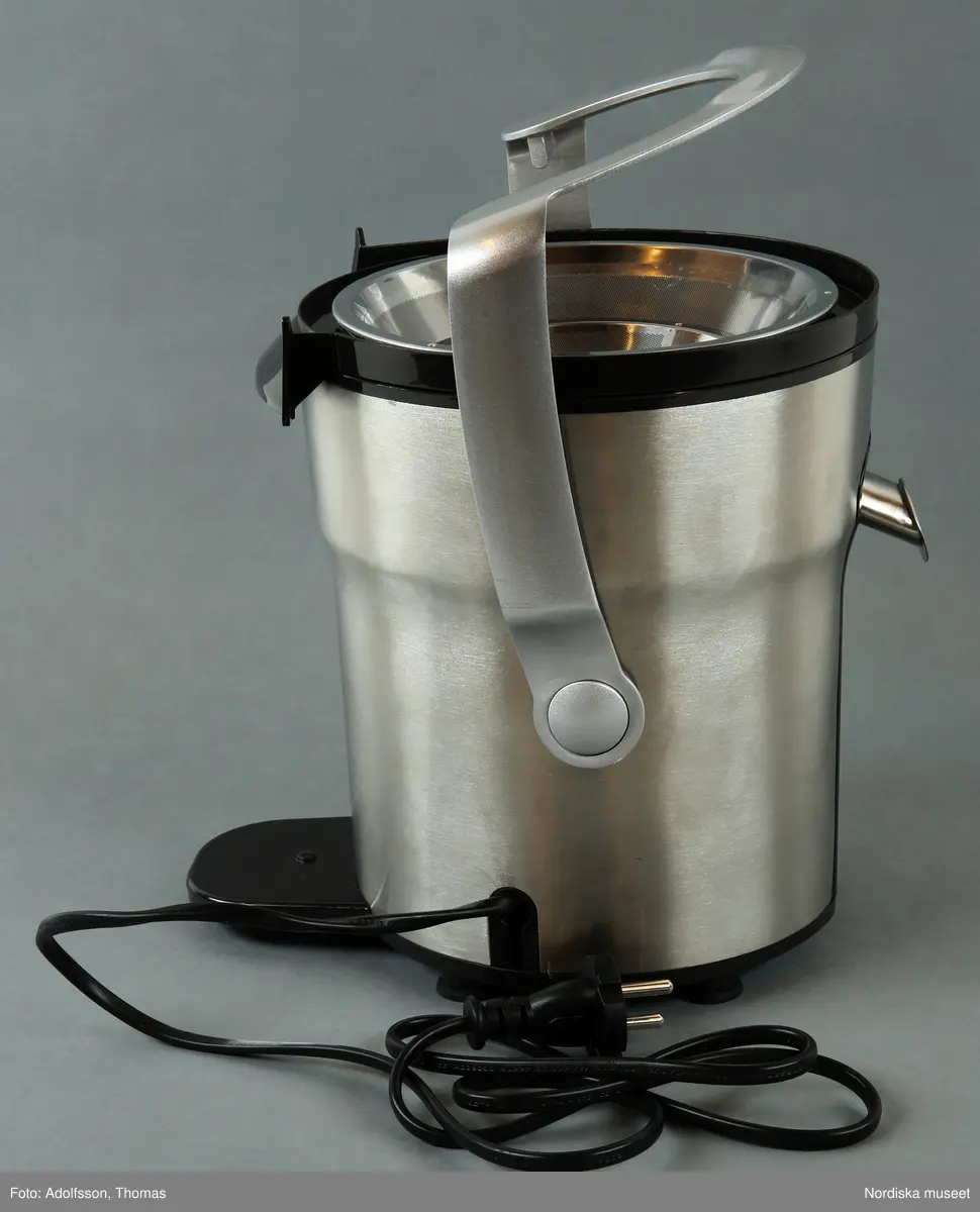 En elektrisk råsaftcentrifug av märket Elektrolux PERFECTJUICE ESF 2000. Består av  6 delar. a) Själva råsaftcentrifugen är cylinderformad och av metall och plast. De övriga delarna är av rökgrå hårdplast och består av b+) ett lock med c) press samt en d) behålllare som fruktköttet samlas i och e) en liten lockförsedd juicekanna med f) skumseparator i form av en plasskena som saften rinner ut i när den är klar. Dessutom en g) bruksanvisningsbroschyr och ett h) garantipapper.
Locket (b+) har en skada där en bit är avslagen.

Lena Kättström Höök 2014-01-10