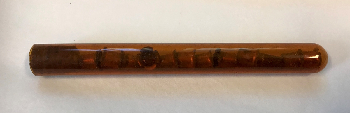 Geologiske prøver og bombedeler. Seks glassrør, en dreid trepropp og en liten beholder i tre. 

Trebeholderen inneholder tre små spisse pinner av ukjent materiale, muligens tennsatser. Et av de brune glassrørene inneholder små metallsylindre. Dette er trolig tennhetter .Et av rørene inneholder en liten glassbit, resten er tomme. Et av rørene er knust.