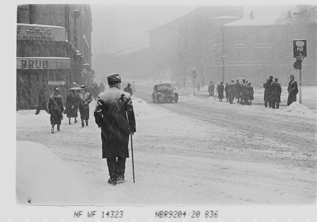 Personer i snøvær på trikkestopp ved Nobelinstituttet, Henrik Ibsens gate, tidligere Drammensveien, Oslo. Fotografert 1941.