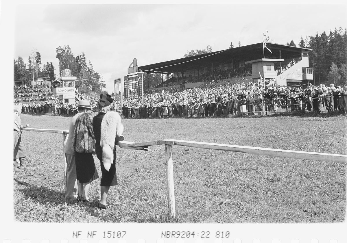 To kvinner med pels på indre bane under løp på Øvrevoll Galoppvane, Bærum. Fotografert 1941.