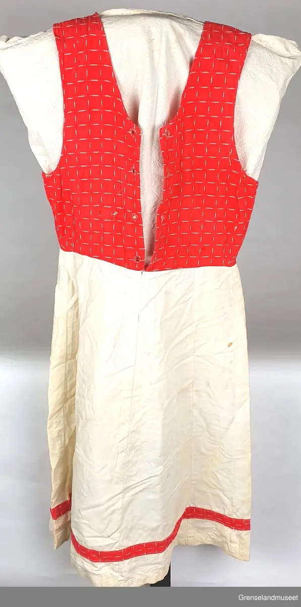 "Hverdagsbunad"  Bomull. 1955.60. Håndsydde huller til snøring i front.
Rødt mønstret liv. Hvitt skjørt med kant av det røde stoffet.