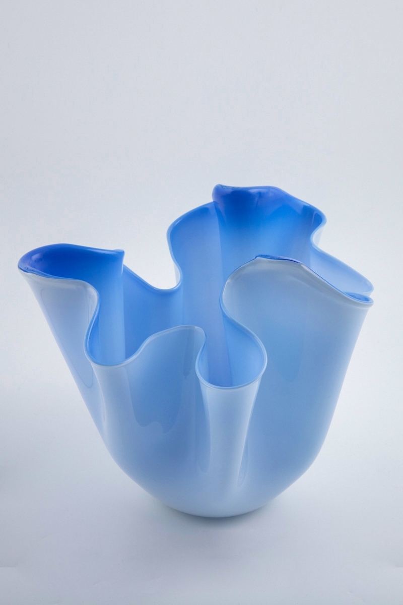 Flerfarget vase i opakt overfangsglass. Yttersiden er melkehvit, mens innersiden er utført i lyseblått glass, hvor den blå fargetonen forsterkes på øvre og nedre del av vavsen. Sirkulær bunn, noe hevet i midten. Vasens nedre del er mykt avrundet, mens øvre del domineres av sterkt dynamiske vegger i ulik høyde, samt bølgende munningsrand.
