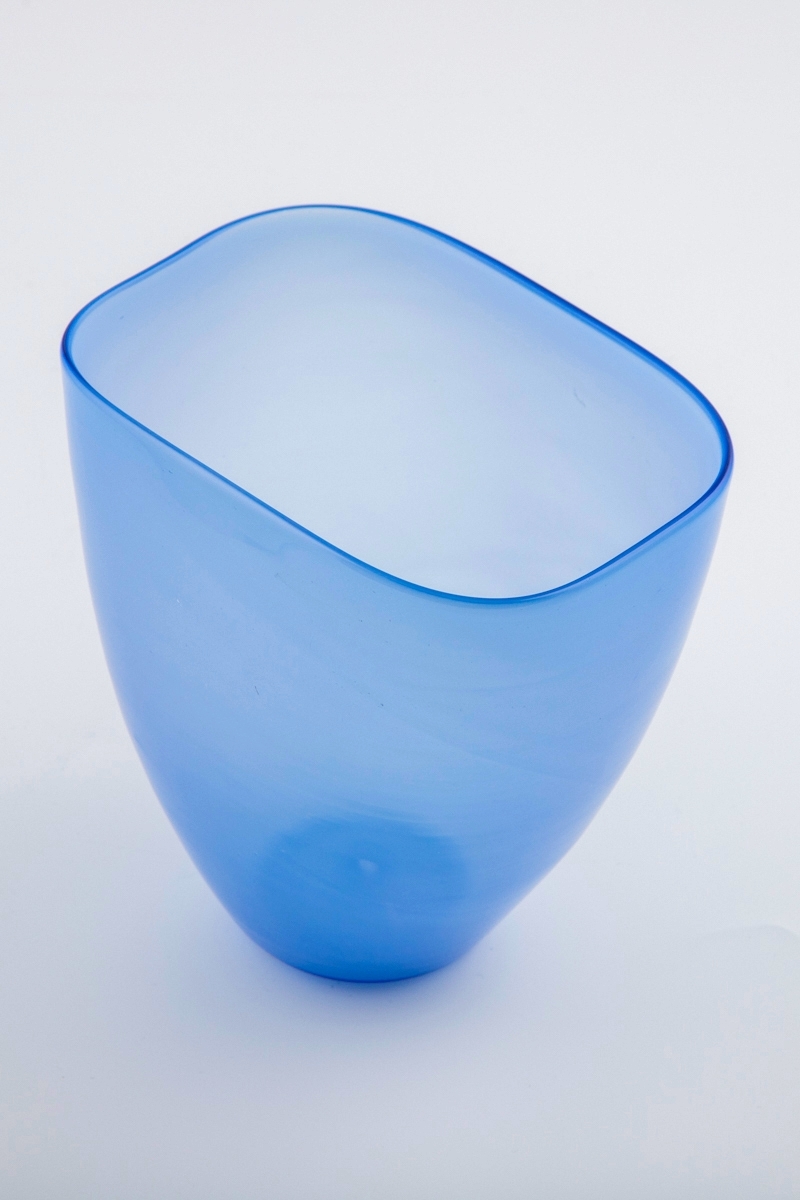 Konisk vase utført i lyseblå opaliserende glassmasse. Korpus hviler på en sirkulær fot, mens munningsranden er rektangulær. Noe hevet bunn med rester av puntemerke.