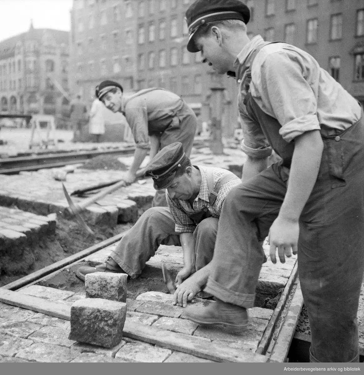 Sporveisarbeidere. Legging av brostein/trikkeskinner på Jernbanetorget. Antatt 1950 - 1955.