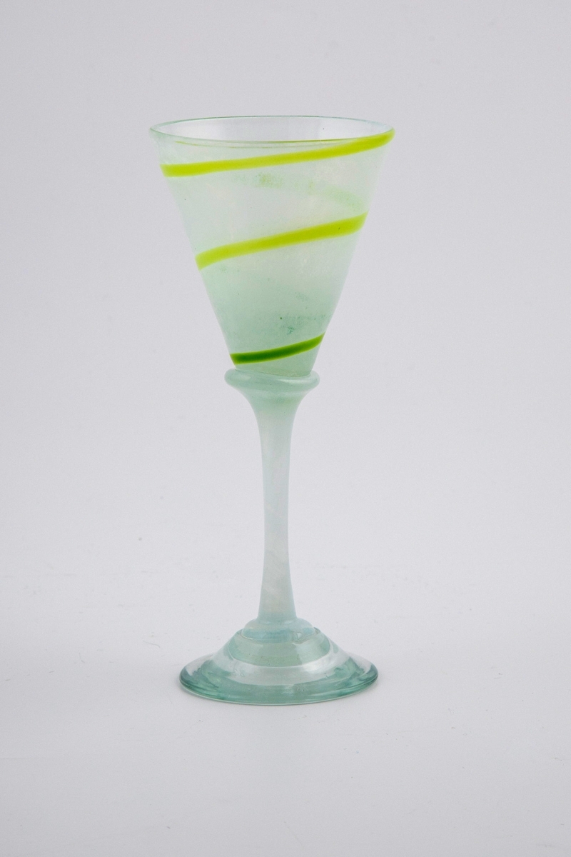 Drikkeglass i halvgjennomskinnelig glass. Kupa er melkehvit og dekorert med en grønn spirallinje. Overgangen til den melkehvite stetten er markert med en skjev vulst. Fotplaten er utført i klart glass.