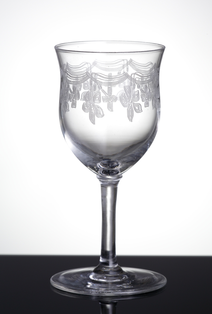 Glas (R.442).
Beskrivning: Pantograferad dekor i form av hängande blomrosetter.
Färg: Ofärgat klarglas.
Mått: Ovan angivna diameter avser glasets fotdiameter.
Inskrivet i huvudkatalogen 1942.
Funktion: Glas