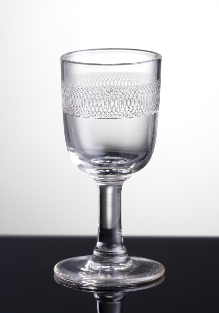 Glas (R.275).
Beskrivning: Guillocherad eller pantograferad bård.
Färg: Ofärgat klarglas.
Mått: Diameter ovan avser glasets fotdiameter.
Inskrivet i huvudkatalogen 1942.
Funktion: Servisglas