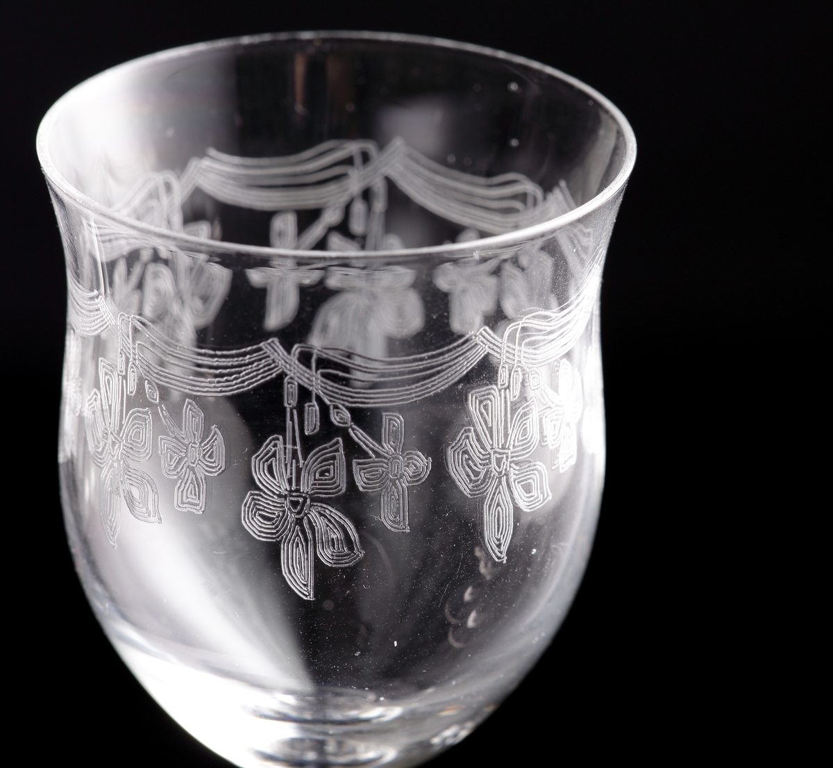 Glas (R.442).
Beskrivning: Pantograferad dekor i form av hängande blomrosetter.
Färg: Ofärgat klarglas.
Mått: Ovan angivna diameter avser glasets fotdiameter.
Inskrivet i huvudkatalogen 1942.
Funktion: Glas