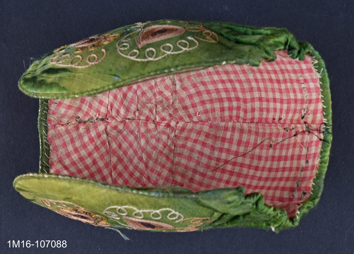 Bindmössa av grönt siden med gulbrunt tambursömsbroderi i bruna nyanser. Bindmössan kopierades till Valledräkten under 1960-talet av ett dräktråd. Har tillhört Carolina Johansson (1835-1917).