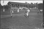 Fotboll. Unga män spelar match. På gaveln av läktaren  på Tranebergs IP står bokstäverna D.I.F; Djurgårdens idrottsförening.