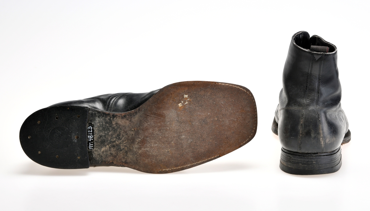 Et par svarte sko/støvler til mann. De er sydd sammen av tre deler av svart skinn. Tåen er svrundet firkantet. På Tåen er det en gjennomhullet skinnbord. Ytterste del av tåen er forsterket. I front er det snøring med 5 par metallmaljer og 4 par metallhekter. De er snøret med flate, svarte skolisser. Under snøringen er det en uforet skinntunge. Skoene er foret med hvitt lerretsstoff. Innersålen er av brunt skinn med forsterkning på hælområdet. Det er tekst på innersålen, men den er delvis slitt bort. Oppe bak på skoen er det en svart og rød lerretshempe sydd på. Skoene er randsydd. Yttersålen er av lær. På hælen er det satt på gummihæl med stift.