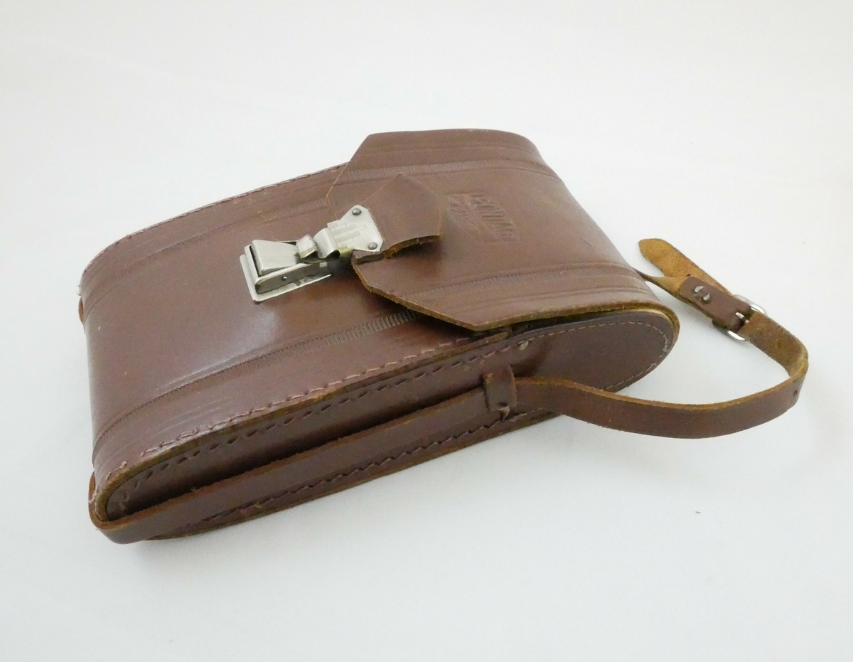 Mørkebrun oval veske i skinn eller lær. Vesken har et bøyd lokk øverst som festet med en metallfeste i enden. Ett bånd i samme materiale som vesken er festet på begge sider, båndet har hakk og en metallfeste til å stramme med. Inne i vesken er det tre gule kartongemballasjer for filmrull, og en bruksanvisning på hvitt papir. 

Påskrift på veske: 
PONTIAC // PARIS
MADE IN PARIS

Påskrift på emballasje: 
KODAK // Tri- X pan // 400