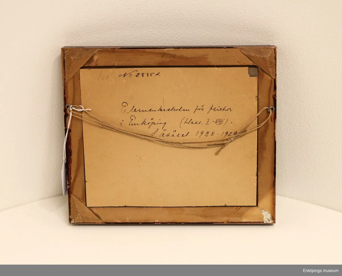 Tavla med inramat fotografi.
Fotografiet föreställer flickor från Elementarskolan för flickor, Enköping, läsåret 1928–29. De står förmodligen på innergården vid gamla Sparbankshuset.
Dr. Ernst Westerlund var initiativtagare till Elementarskolan för flickor. Skolan startades den 1 september 1885. Dr. Westerlund donerade skolmaterial, möbler, hyrde skollokal och donerade pengar till skolan. Han var även hälsoansvarig på skolan och gav eleverna kostnadsfri sjukvård. Skolan lades ned 1935.
Den sista bilden visar ett tidningsurklipp från Enköpings-Posten den 8 juni 1886 där dessa fakta framkommer.