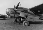 Flygplan Saab B 18 står på ett flygfält, 1940-tal. En person arbetar med flygplanet. Flygplanet är märkt 'Gunnel'. I bakgrunden står ett flygplan B 3 Junkers Ju 86K tillhörande F 14 Hallands flygflottilj.