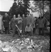 Folksamling med män och kvinnor på baksidan av Brahegatan 75a (Hjertströmska gården). Pastor Robert Svensson tar första spadtaget till Filadelfiakyrkan. Till vänster om pastorn står Harry Forsberg, därefter Abel Svensson, Sven Bardh, Erik Olofsson, Sven Richardsson samt Edvin Andersson.