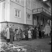 En grupp män och kvinnor på baksidan av Brahegatan 75a (Hjertströmska gården) står och sjunger till ackompanjemang av en kvinna som spelar dragspel. Närmast i bild står pastor Robert Svensson