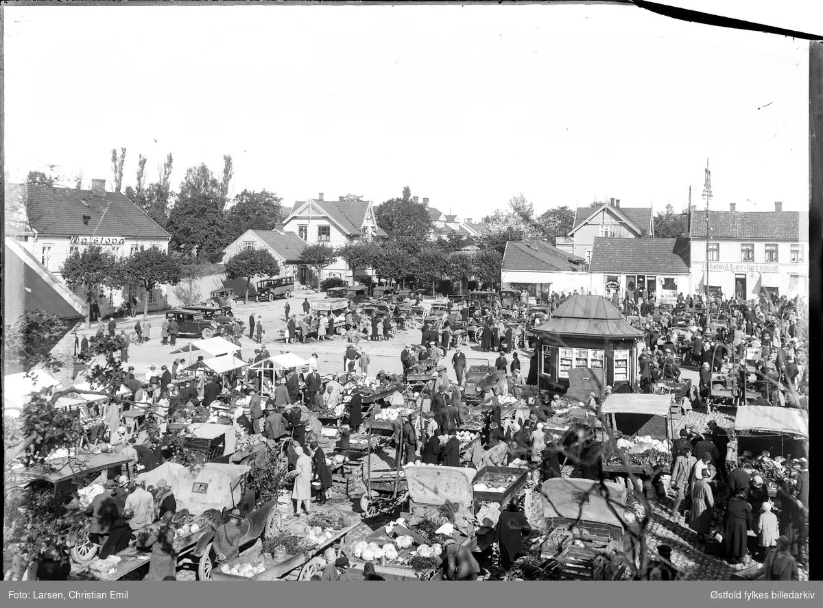 Sarpsborg torg, oversiktsbilde 1930. Matstova til Bondeungdomslaget venstre.
Skotøi- og Lærforretning. 
Bilen med kjennetegn nr. B-1610 til venstre for aviskiosken er en Ford T  1920-22-modell. Eier iflg. Bilboken for Norge 1930 var da Josefine Øistad, Skjeberg. Bil med lys kalesje i forgrunnen til venstre er også en Ford T.