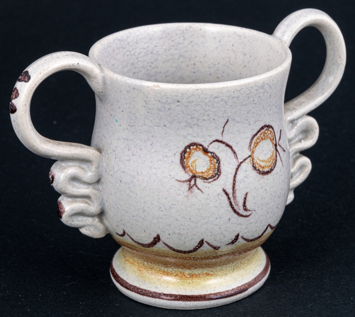 Bägare av lergods. Bo Fajans, design Eva Jancke­Björk. Grå S­svängd med stora hänklar, ljus- och mörkbruna partier nedtill samt dekor av en blomma.