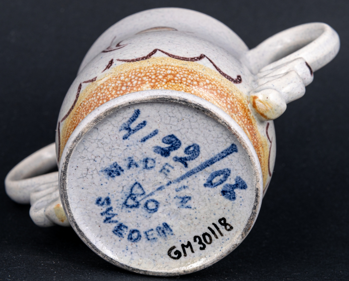 Bägare av lergods. Bo Fajans, design Eva Jancke­Björk. Grå S­svängd med stora hänklar, ljus- och mörkbruna partier nedtill samt dekor av en blomma.