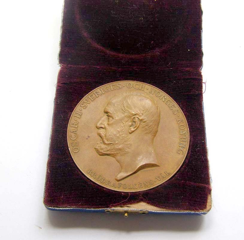 Minnesmynt från Stockholmsutställningen 1897.
Myntet är av brons, och visar på ena sidan en profilbild av Oscar II i halvrelief. På den andra sidan syns en halvnaken kvinnofigur hållande ett palmblad (?) i ena handen och en lagerkrans i den andra handen.
Text på ena sidan: "Oscar II Sveriges och Norges konung - Brödrafolkens väl".
Text på andra sidan: "Allmänna konst och industriutställningen i Stockholm 1897".

Myntet förvaras i en tillhörande ask fodrad med brun sammet.