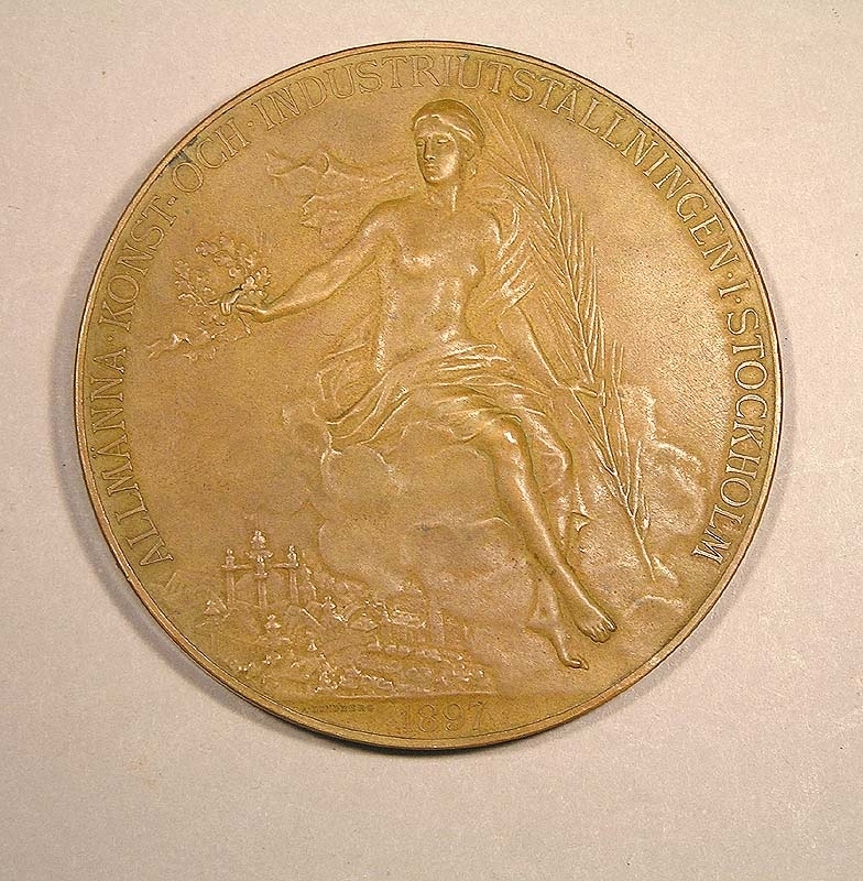 Minnesmynt från Stockholmsutställningen 1897.
Myntet är av brons, och visar på ena sidan en profilbild av Oscar II i halvrelief. På den andra sidan syns en halvnaken kvinnofigur hållande ett palmblad (?) i ena handen och en lagerkrans i den andra handen.
Text på ena sidan: "Oscar II Sveriges och Norges konung - Brödrafolkens väl".
Text på andra sidan: "Allmänna konst och industriutställningen i Stockholm 1897".

Myntet förvaras i en tillhörande ask fodrad med brun sammet.