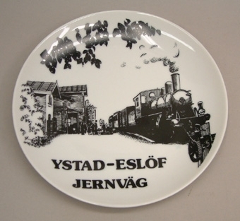 Vit porslinstallrik med svart dekor. Text: "YSTAD-ESLÖF JERNVÄG"
På tallriken visas Äsperöd station med tåg omkring 1917. Stationer av liknande typ finns utmed Y.E.J. i Hurva, Löberöd, Lövestad och Svenstorp.

Ystad är en av de platser som tidigarenämns i samband med järnvägsanläggningar i Sverige. När greve A. E. von Rosen år 1845 til regeringen inlämnade ett förslag om järnvägar, upptog han nämligen Ystad som ändpunkt för en huvudlinje från Stockholm över Tisnaren och Eksjötrakten.