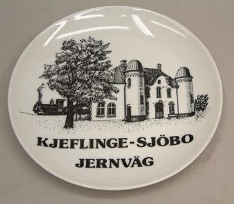 Vit porslinstallrik med svart dekor. Illustrationen visar Harlösa station. Text: "KJEFLINGE-SJÖBO JERNVÄG"

Denna tallrik har utgivits i 100 numrerade ex. av vilka detta är nr.1.
Harlösa station blev indragen 1955. Efter att ha stått tomt i några år
flyttade SJ:s luftledningsskola in i byggnaden och stationsområdet utrust-
ades med elektriska luftledningar etc. för undervisningsändamål.