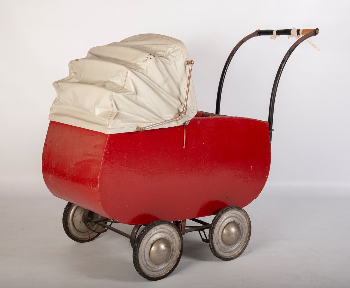 Rødmalt vogn med gråmalt innerside og lys grå kalesje av kunstlær. 4 metallhjul med nedslitt gummidekk. Håndtak av tre med svart plastlignende materiale som er sprøtt. Kalesje med ei flenge. Polstret karm. Mangler skrue i håndtak og kalesje.
