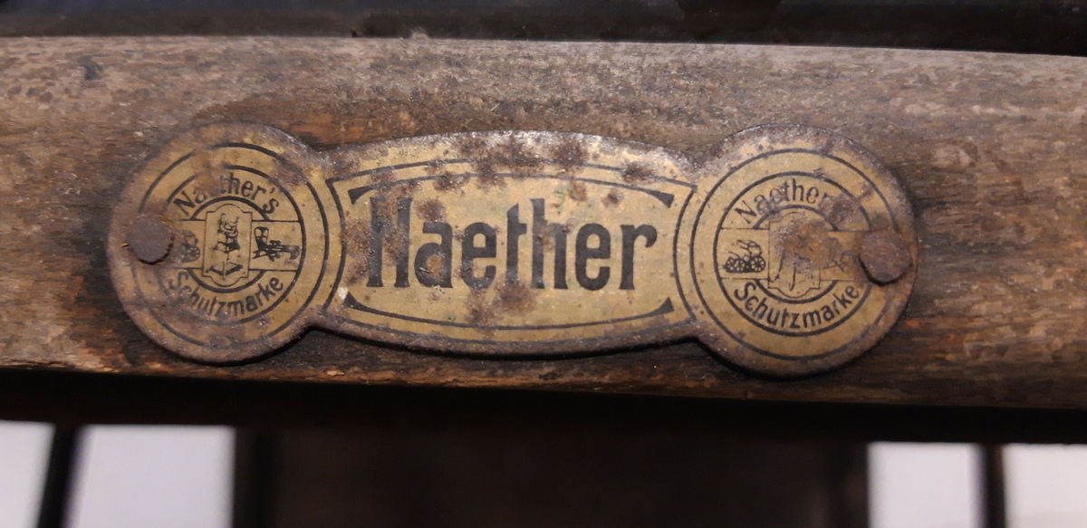Ramme av tre med kunstlær i sete og rygg. Håndtak av jernrør. 4 hjul mangler dekk. Mangler stopper for fotbrett. Hull i ryggtrekket og mye rust. Setetrekket løsnet i den ene siden. noen enkle reparasjoner med ståltråd.