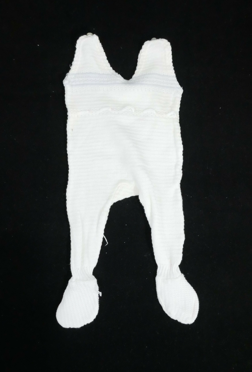 Sparkebukse med påsydde føtter. En knapp på hver skulder. Dekor med blå bord på midten foran og bak. Pikotkant rundt halsen og ermeåpningene, i livet er det snøring. Mønsterstrikk over hele buksa. 