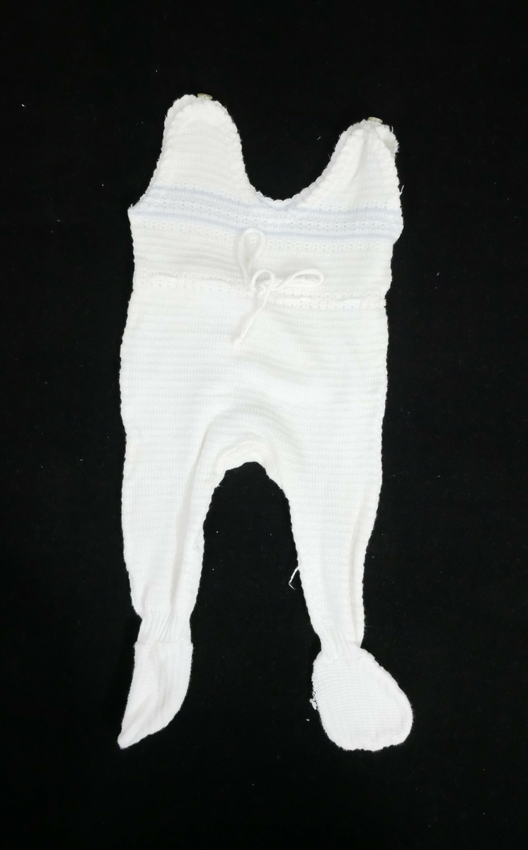 Sparkebukse med påsydde føtter. En knapp på hver skulder. Dekor med blå bord på midten foran og bak. Pikotkant rundt halsen og ermeåpningene, i livet er det snøring. Mønsterstrikk over hele buksa. 