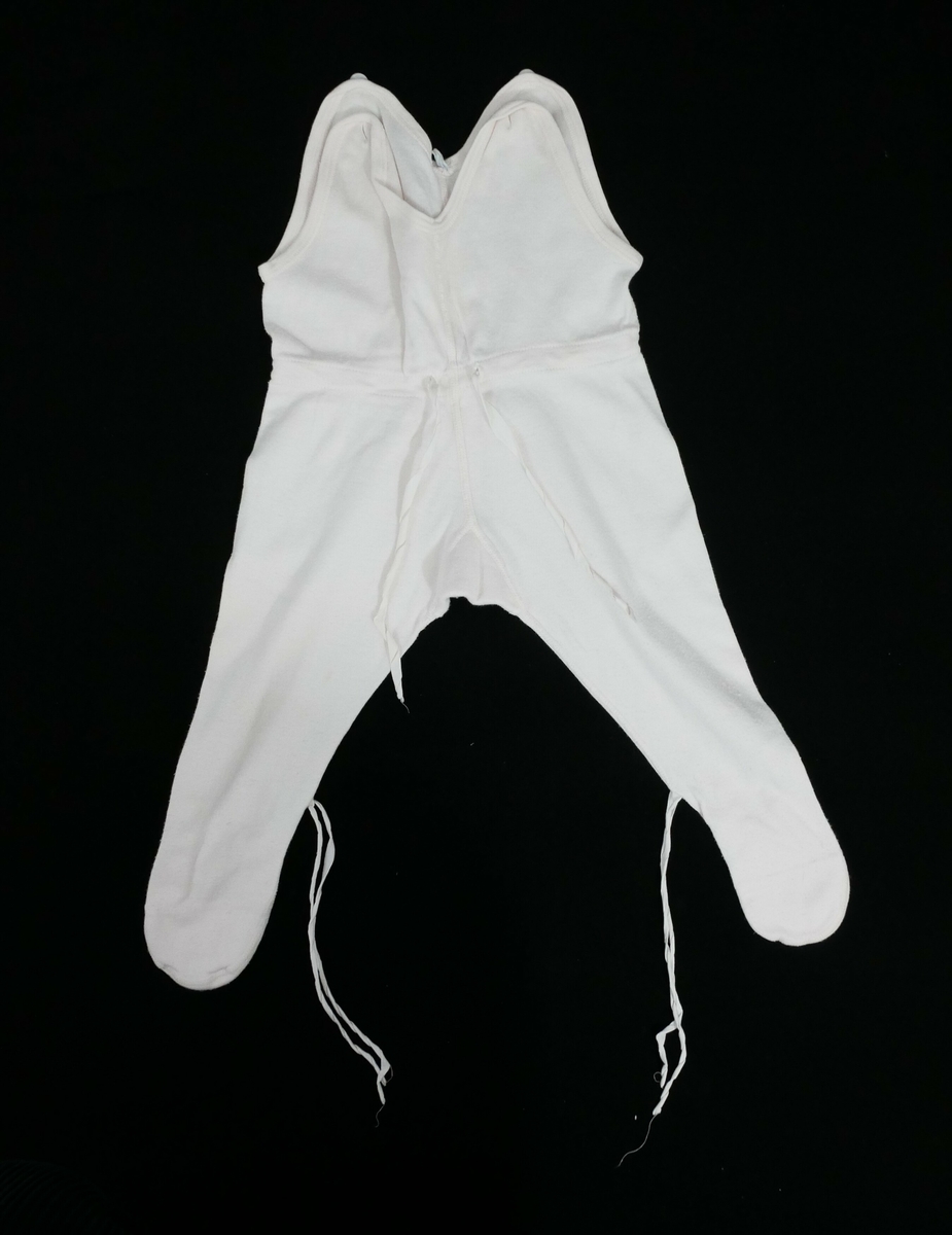 Sparkebukse med påsydde føtter. En knapp på hver skulder. Snøring i livet og i føttene med rosa tråd. 

Påskrift, vaskelapp: 
NORSK 65 // ekte  // DUUN // FRA JANUS // BOMULL