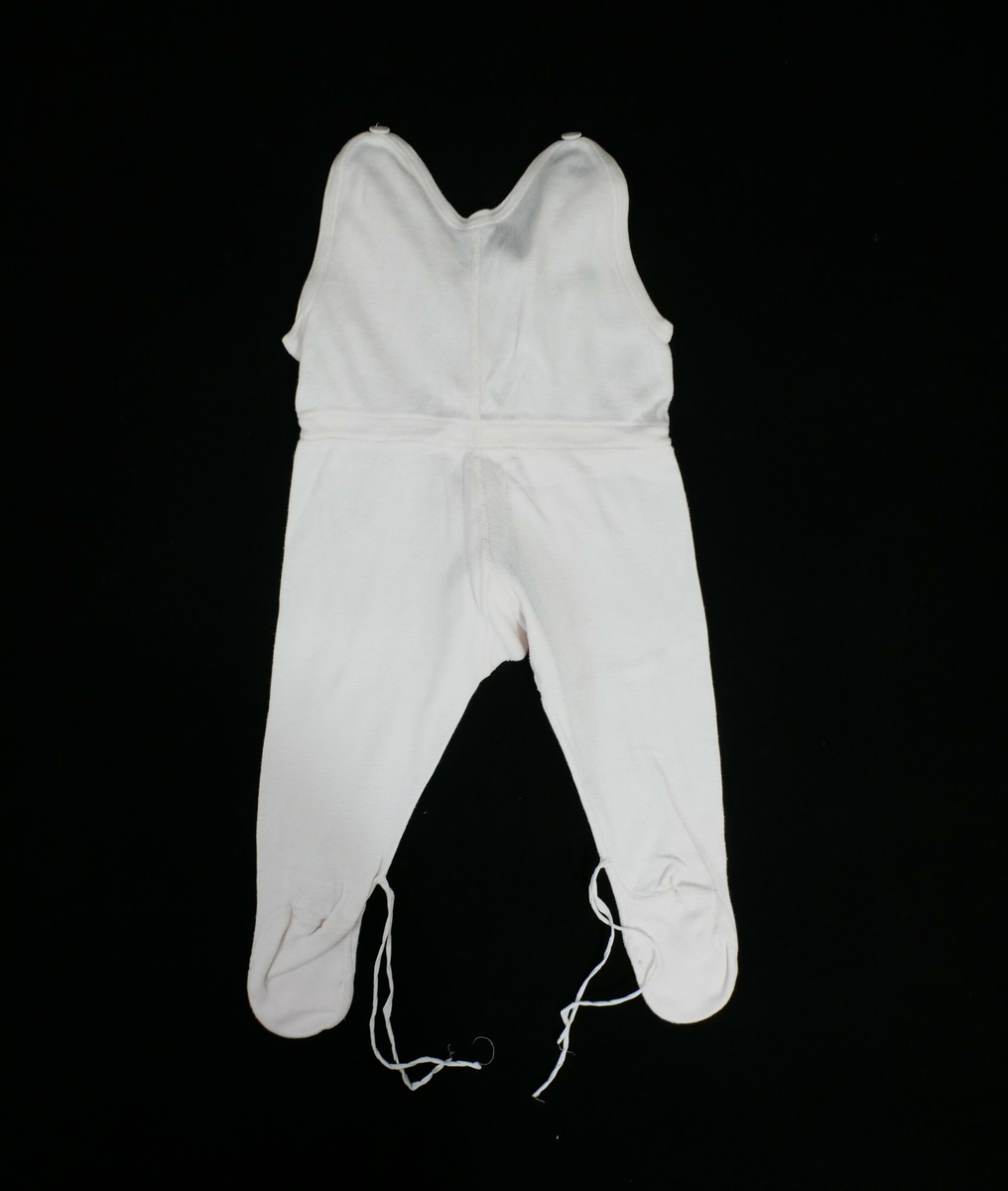 Sparkebukse med påsydde føtter. En knapp på hver skulder. Snøring i livet og i føttene med rosa tråd. 

Påskrift, vaskelapp: 
NORSK 65 // ekte  // DUUN // FRA JANUS // BOMULL