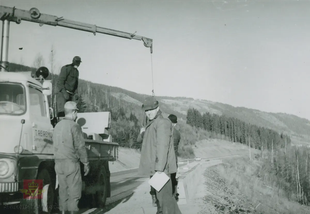 Nedsetting av kantstein høsten 1965. "T. Reiremo Sementvarefabrikk Lillehammer." Mannen fremst på bildet tilhørte Reirmo. Lastebilen med kjennetegn E-12632  er en engelskbygd Ford Thames Trader FC, som var i produksjon 1957-65. FC sto for Forward Control/dvs. bulldog/halvbulldog, med et meget karakteristisk design av frontpartiet. Se: Asbjørn Rolseth: Norsk Lastebilleksikon bind II (1940-1990) s. 132-134. Lastebil med kjennetegn E-12632. Opplysninger om kjøretøyet fra Ivar E. Stav.